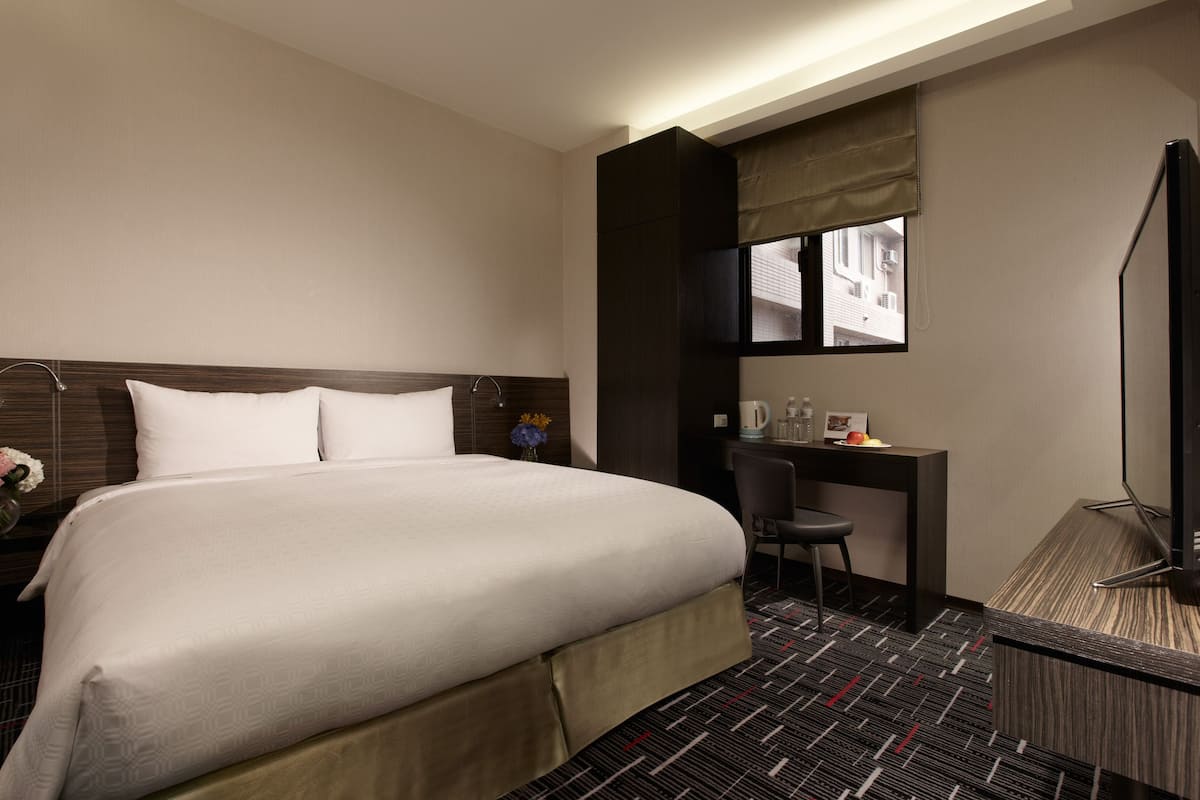 A hotel room with a large bed, a desk, a chair, and a television.