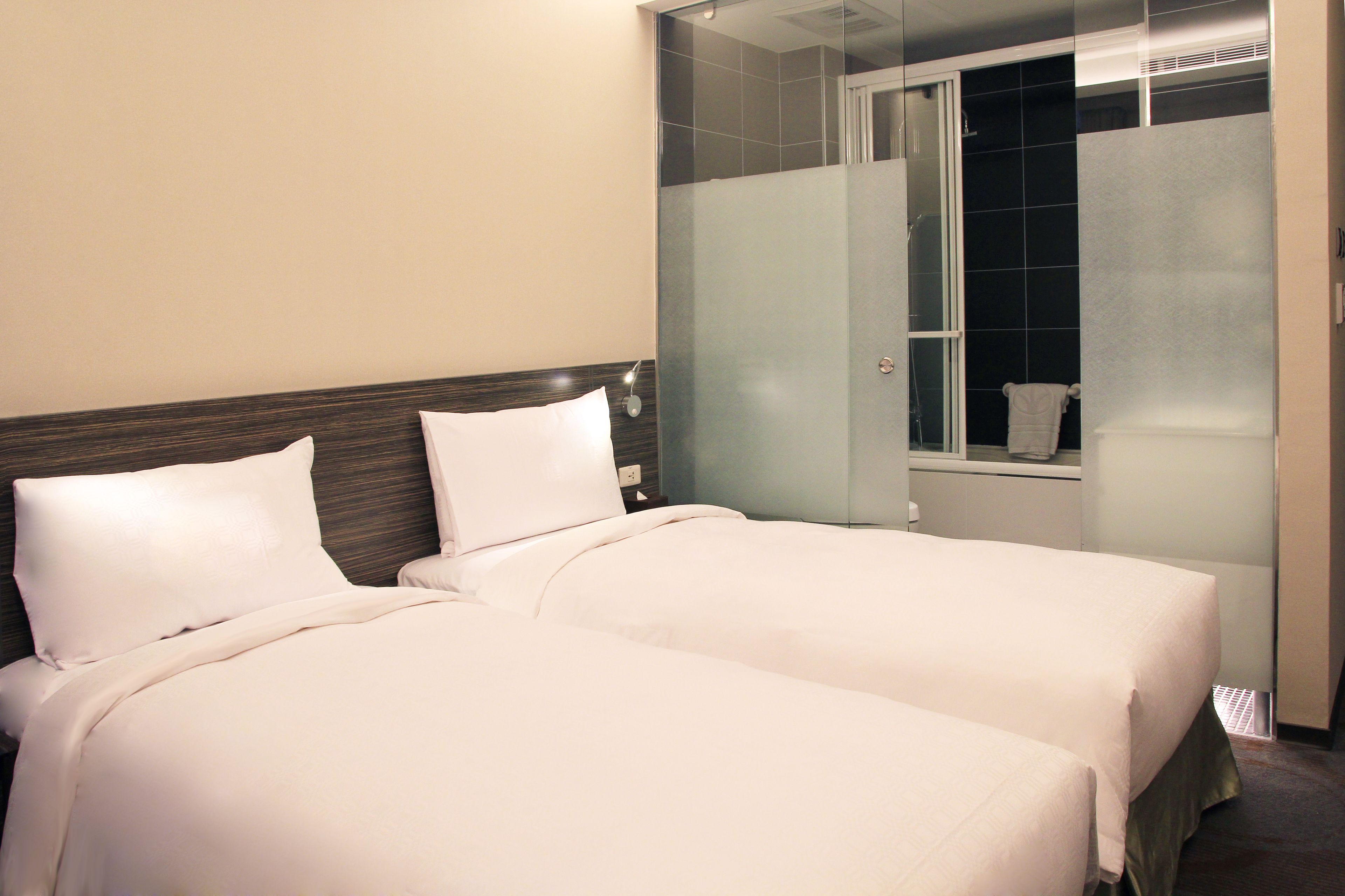 Een hotelkamer met twee bedden, een houten hoofdeinde en een douchecabine met glazen wanden.
