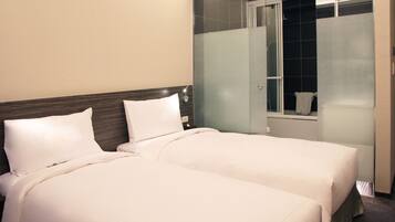 Een hotelkamer met twee bedden, een houten hoofdeinde en een douchecabine met glazen wanden.
