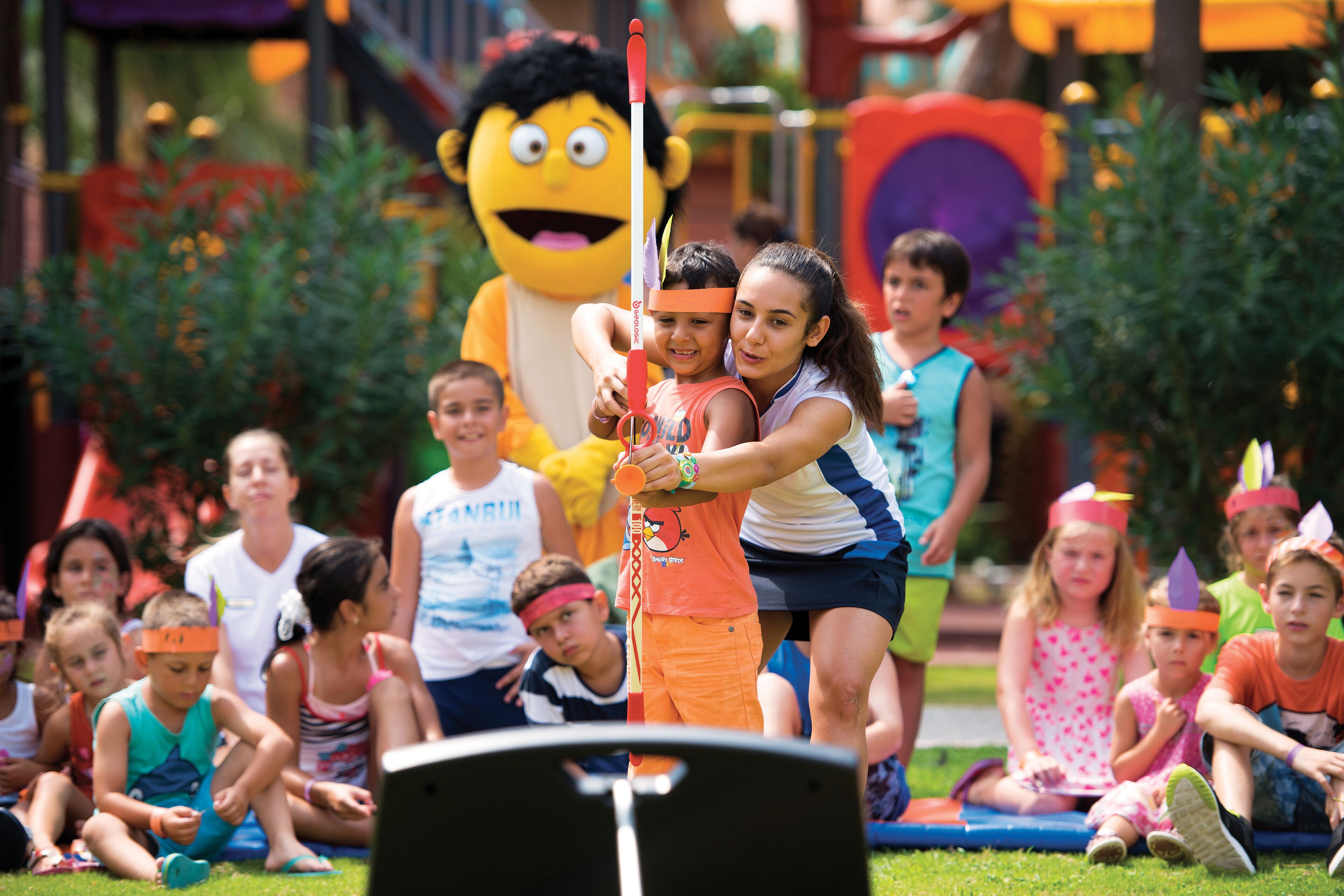 A group of children playing with a mascot in a park.