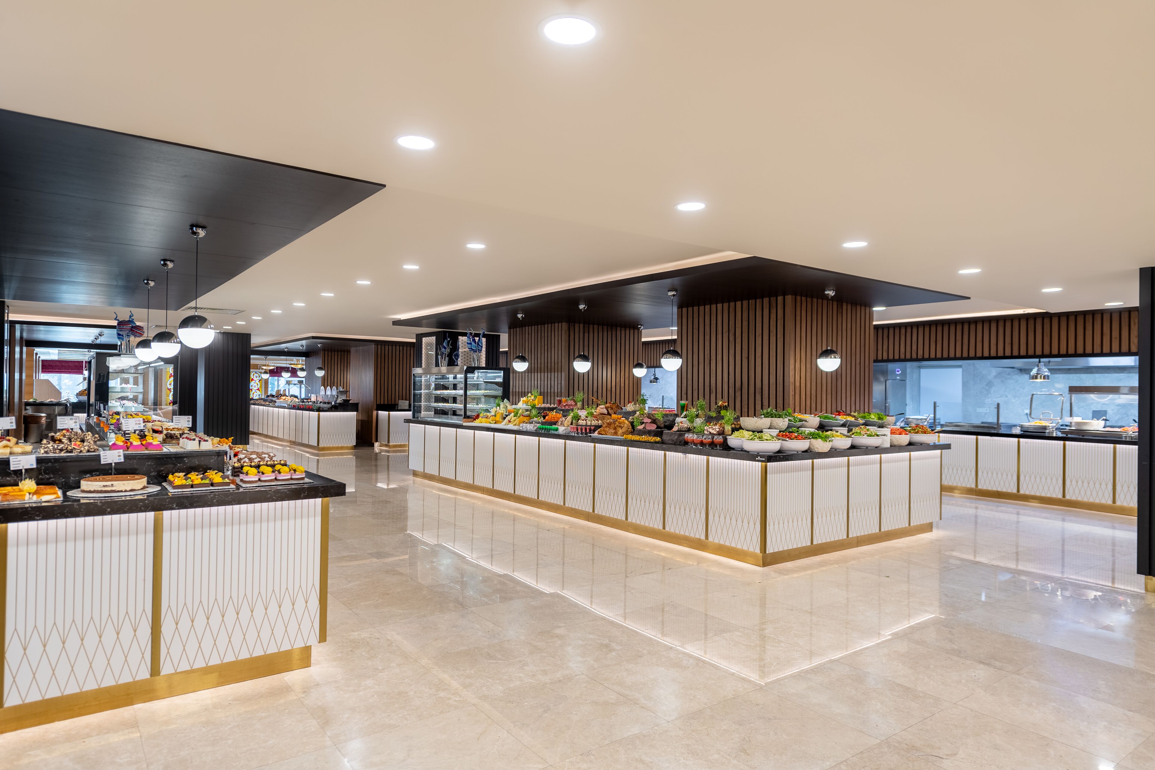 Eine moderne Hotelhalle mit einer zentralen Insel, die ein Buffet beherbergt, umgeben von Sitzbereichen und einer hohen Decke mit eingelassener Beleuchtung.
