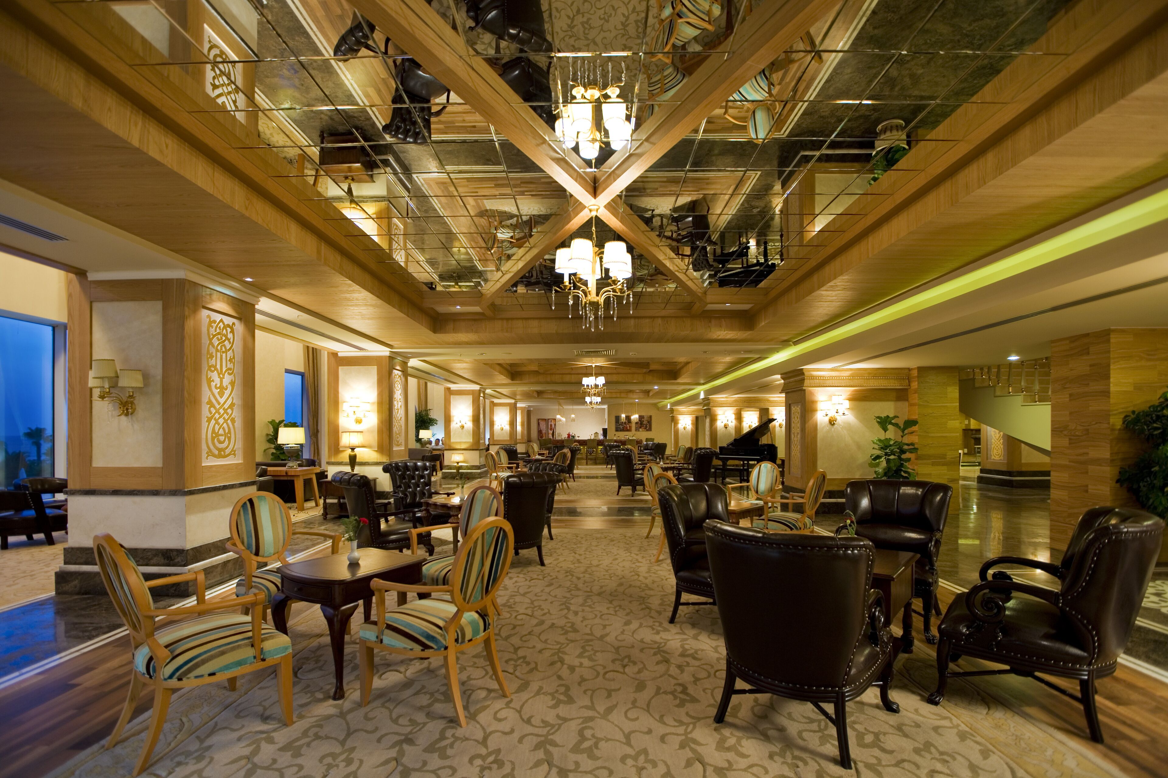 A spacious lobby with a grand chandelier, wooden ceiling beams, and a piano.