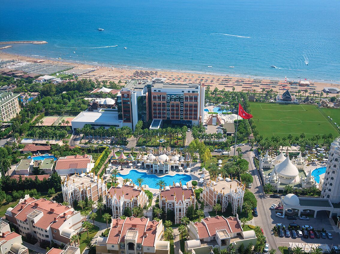 An aerial view of a resort with a large pool, multiple buildings, and a beach.