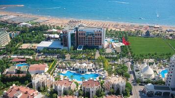 An aerial view of a resort with a large pool, multiple buildings, and a beach.