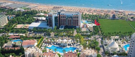 An aerial view of a resort with a large pool, multiple buildings, and a beach.