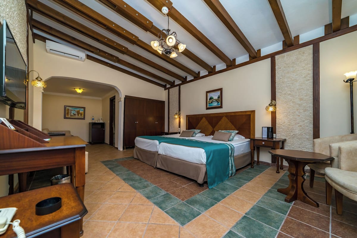 A hotel room with a large bed, a desk, a chair, a small table, and a ceiling fan.