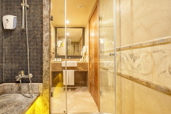 Un baño moderno con cabina de ducha de vidrio, pared con azulejos de mármol y tocador con espejo.