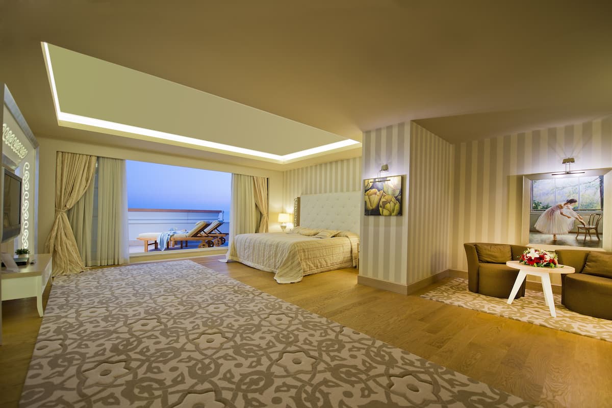 A hotel room with a large bed, a sofa, a small table with flowers, a painting, and a view of the sea.