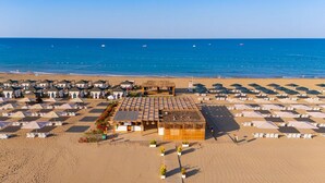 A beach with rows of sunbeds and umbrellas, a central building with a thatched roof, and the sea in the background. - Kamelya Selin Hotel Luxury Resort & SPA (Manavgat)