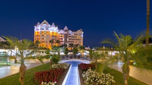 A hotel with a central water feature, surrounded by well-maintained gardens and palm trees.