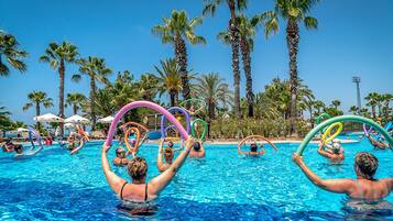 Una piscina con gente sosteniendo aros de colores, rodeada de palmeras y sombrillas.