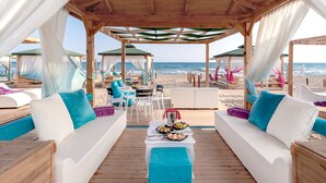 A beachside lounge with wooden flooring, white cushioned seating, and a table with food.