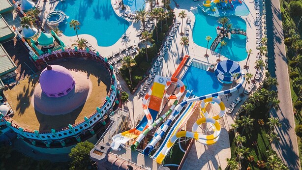 An aerial view of a resort with multiple swimming pools, a water park, and a large circular building.