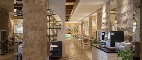 A hotel lobby with a long reception desk, seating area, and a coffee station.