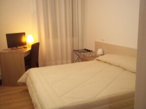 Ein Hotelzimmer mit Bett, Schreibtisch mit Lampe und Fernseher.