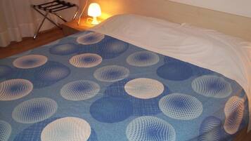 Un lit recouvert d’une couvre-lit aux motifs circulaires bleus et blancs, un oreiller blanc et une lampe de chevet posée sur une table de nuit en bois.