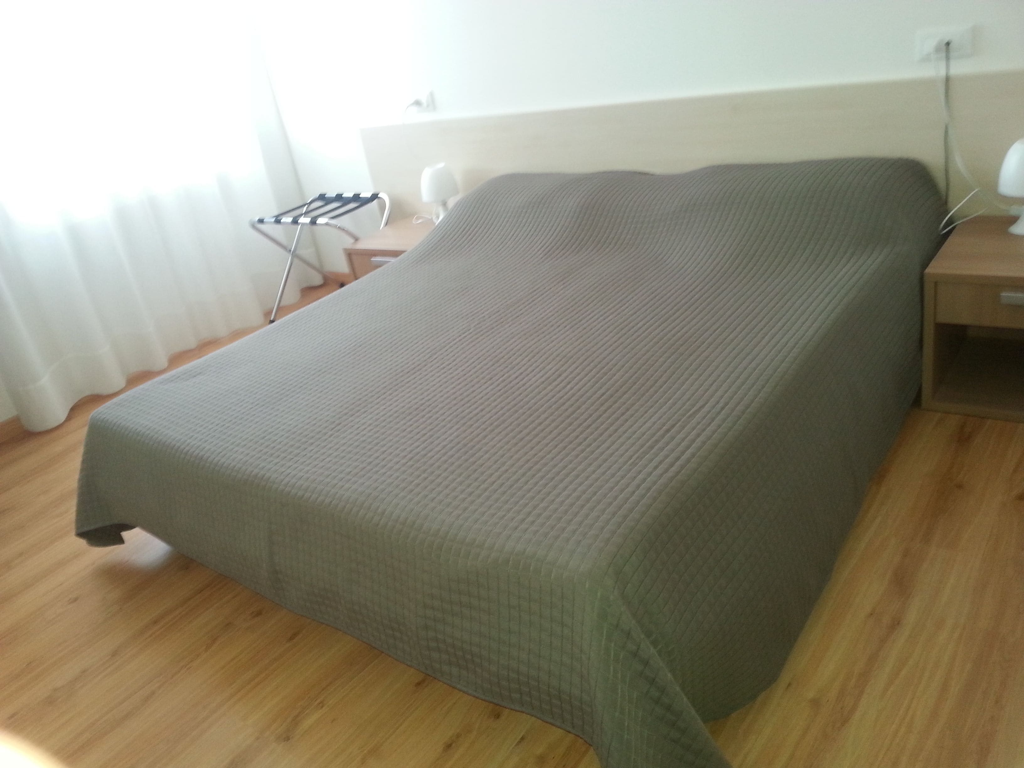 Un dormitorio con cama, suelo de madera, mesita de noche y tocador.