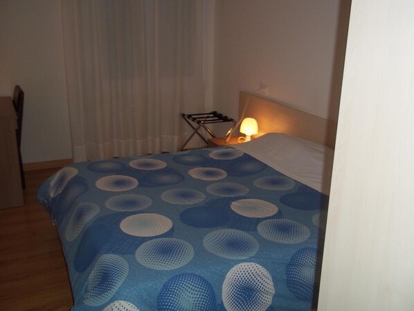 Una habitación de hotel con cama, una mesita de noche con lámpara y una ventana con cortinas.