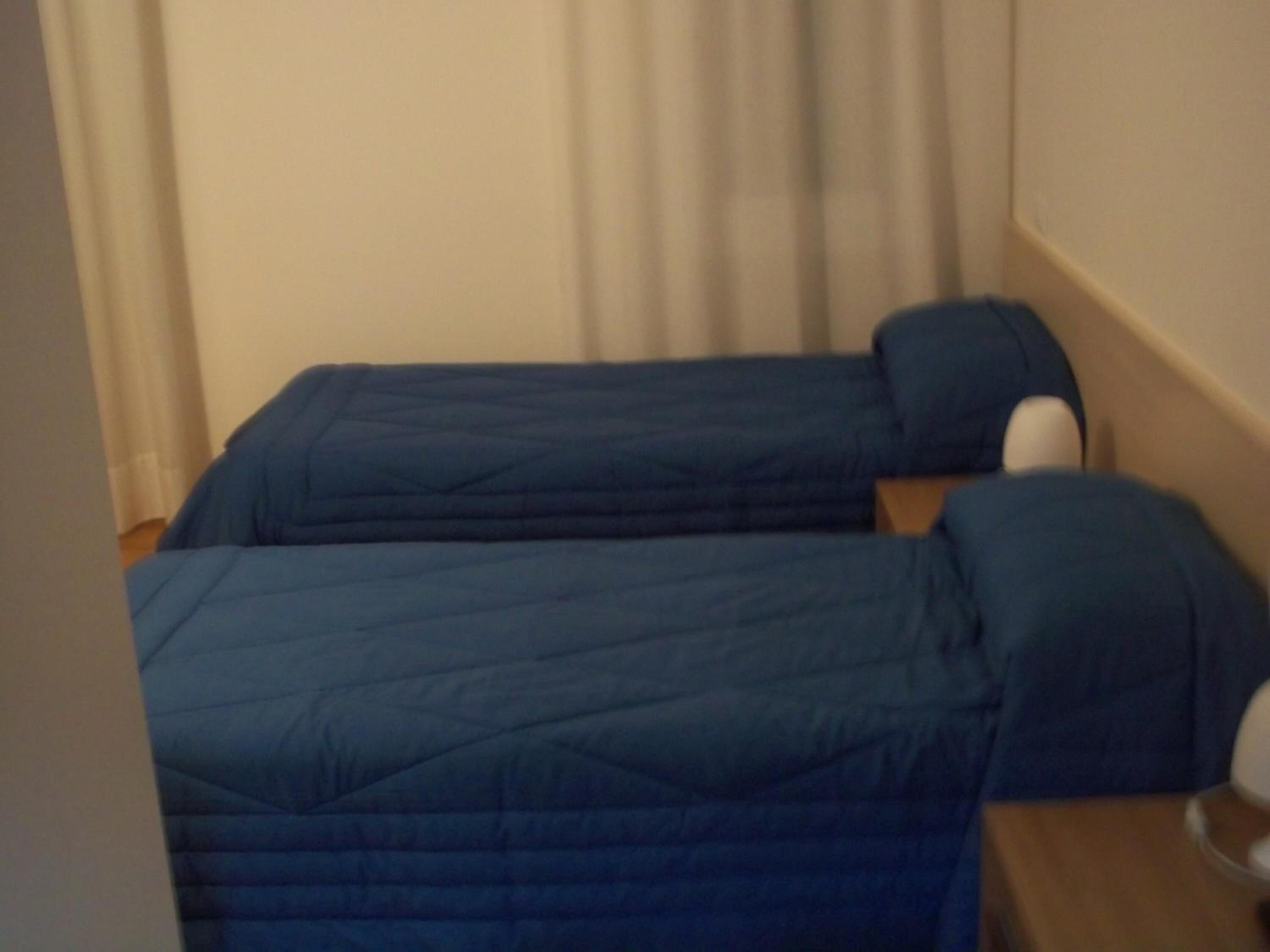 A room with two single beds, each with a blue mattress and matching pillow.
