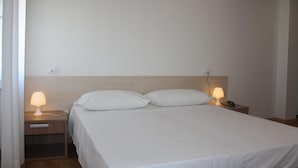 A neatly made bed with white linens, two bedside lamps, and a wooden nightstand.