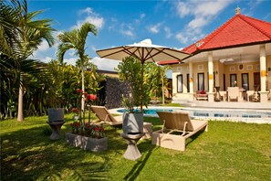 A poolside area with lounge chairs, a large umbrella, and a pool. - Bali Asih Villa (Kerobokan)