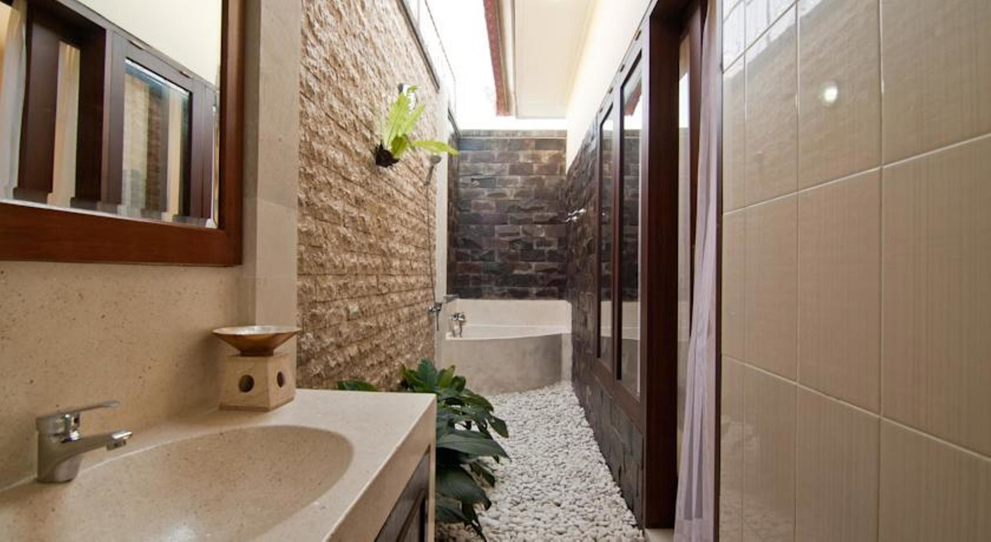 A narrow bathroom with a stone wall, a bathtub, and a sink.