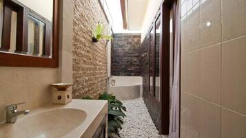A narrow bathroom with a stone wall, a bathtub, and a sink.