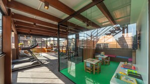 A modern indoor space with a treadmill, children's play area, and large windows offering views of the outside. - Hotel Laghetto Stilo Centro (Gramado)