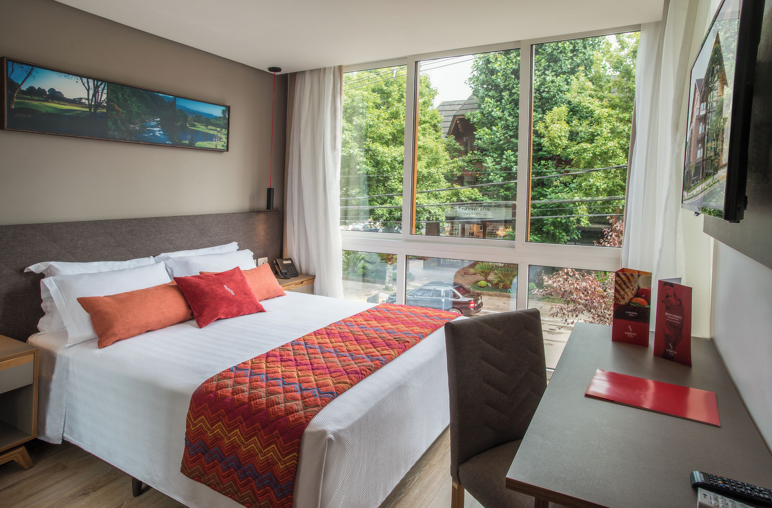 Habitación de hotel con una cama grande, un escritorio y vistas al exterior con vegetación.