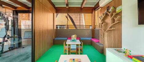 A room with a green carpet, a white table, and a wooden bench. There is a window with a view of a building outside.