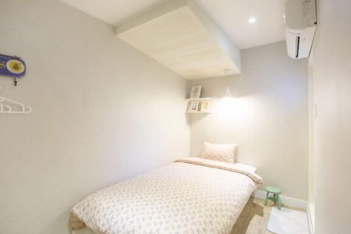 A bedroom with a bed, a small stool, and a shelf with items.