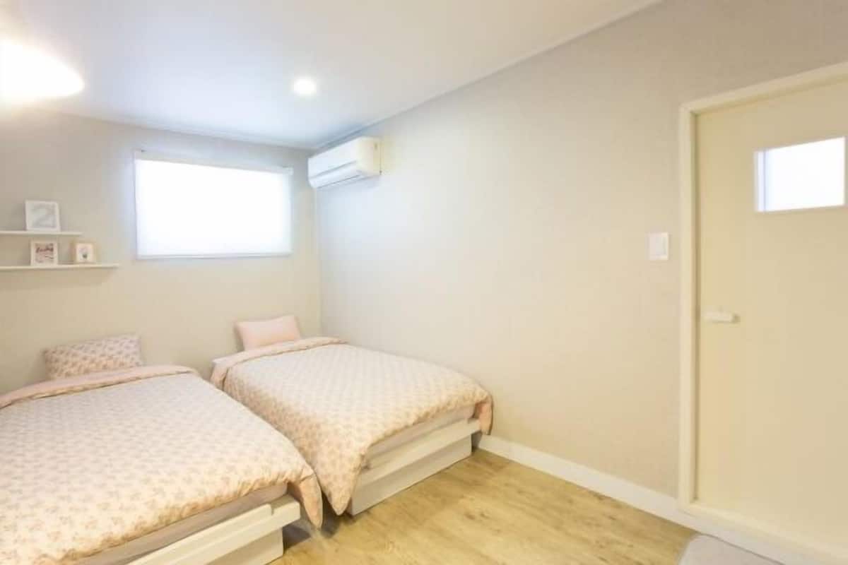 A small, single-room apartment with two beds, a window, and a door.
