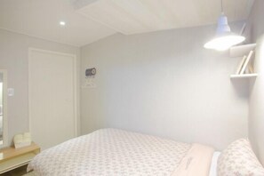 A bedroom with a bed, a bedside table, a hanging light fixture, and a door. - Hostel Vanilla 1 Dongdaemun (Seoul)