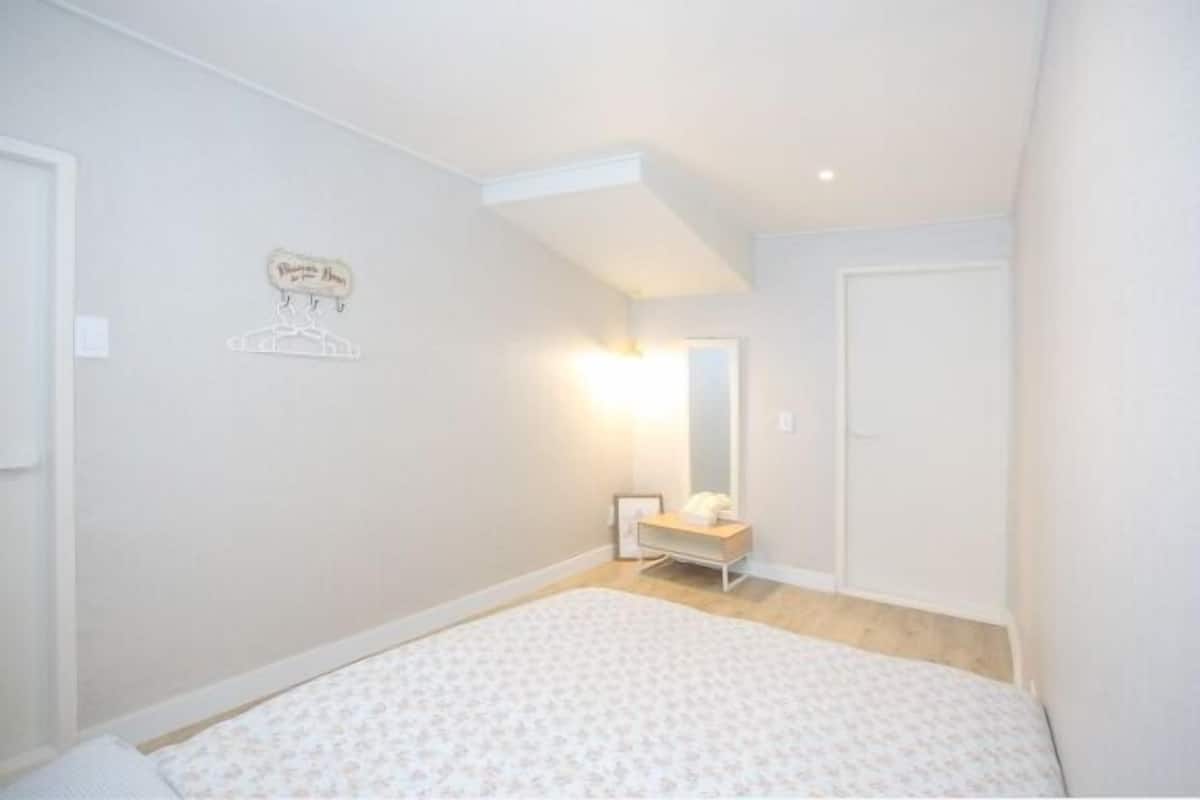 A bedroom with a bed, a bedside table, a mirror, and a wall-mounted light fixture.