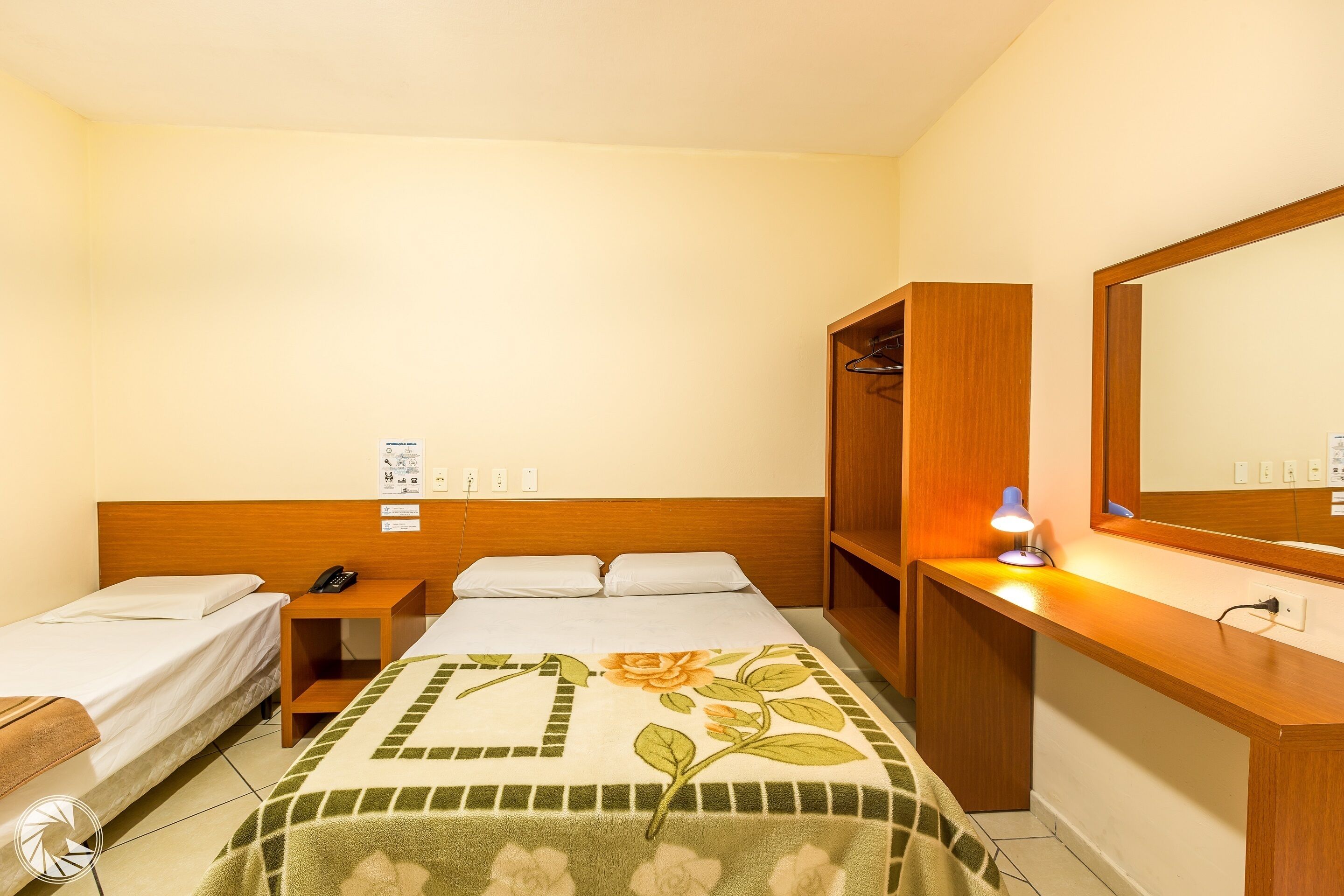 A hotel room with a bed, a desk with a lamp, a wardrobe, and a mirror.