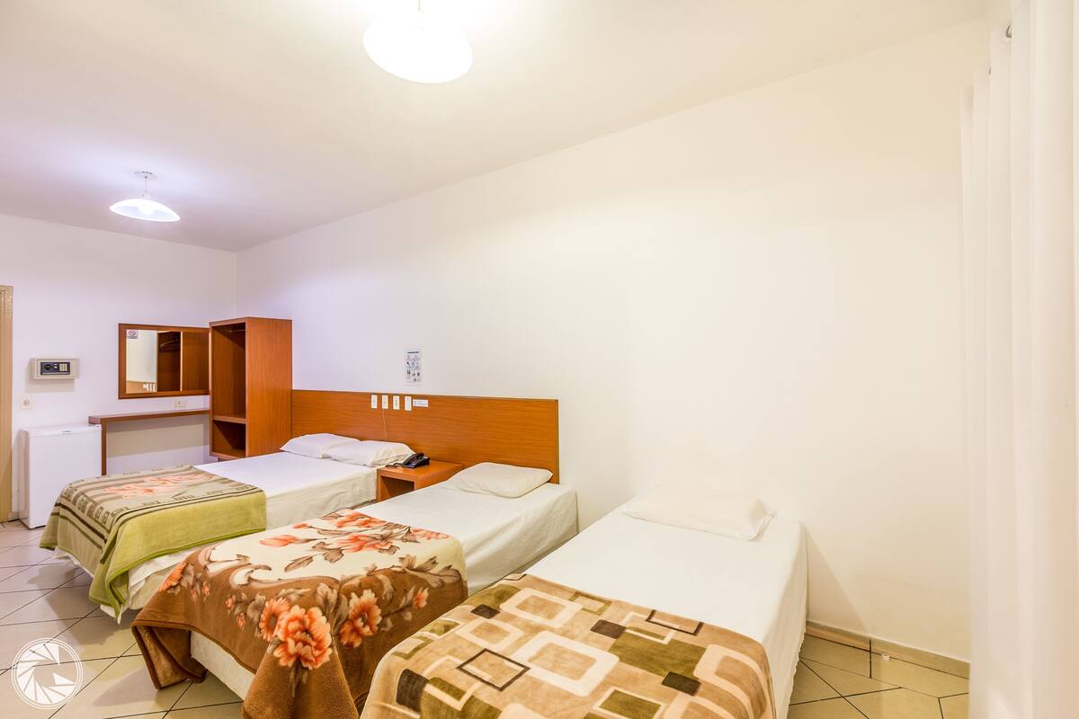 Una camera d'albergo con tre letti singoli, un armadio in legno, una scrivania e uno specchio a parete.