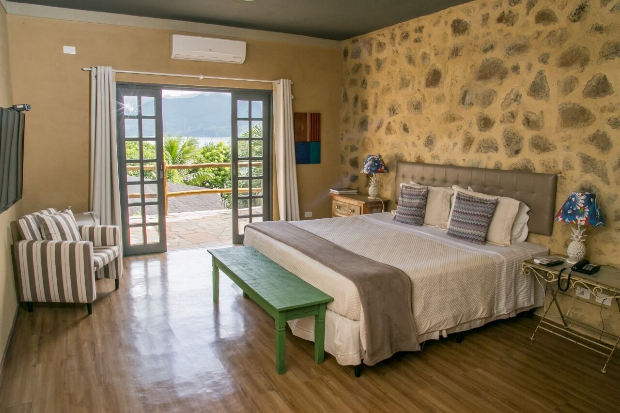 A bedroom with a bed, a bench, a nightstand, and a view of the outdoors.