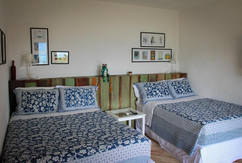 A hotel room with two beds, each with a floral-patterned bedspread. There are framed pictures on the wall, a small table between the beds, and a green decorative headboard.