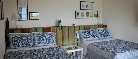 A hotel room with two beds, each with a floral-patterned bedspread. There are framed pictures on the wall, a small table between the beds, and a green decorative headboard.