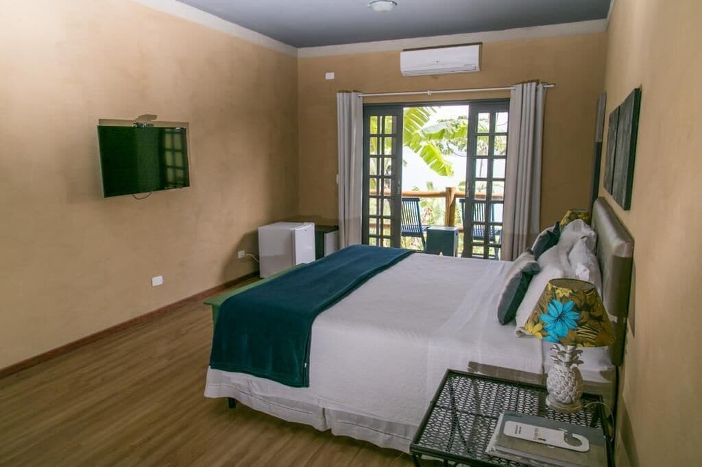 Ein Schlafzimmer mit einem Bett, einem kleinen Tisch, einem Fernseher und einem Fenster mit Vorhängen.