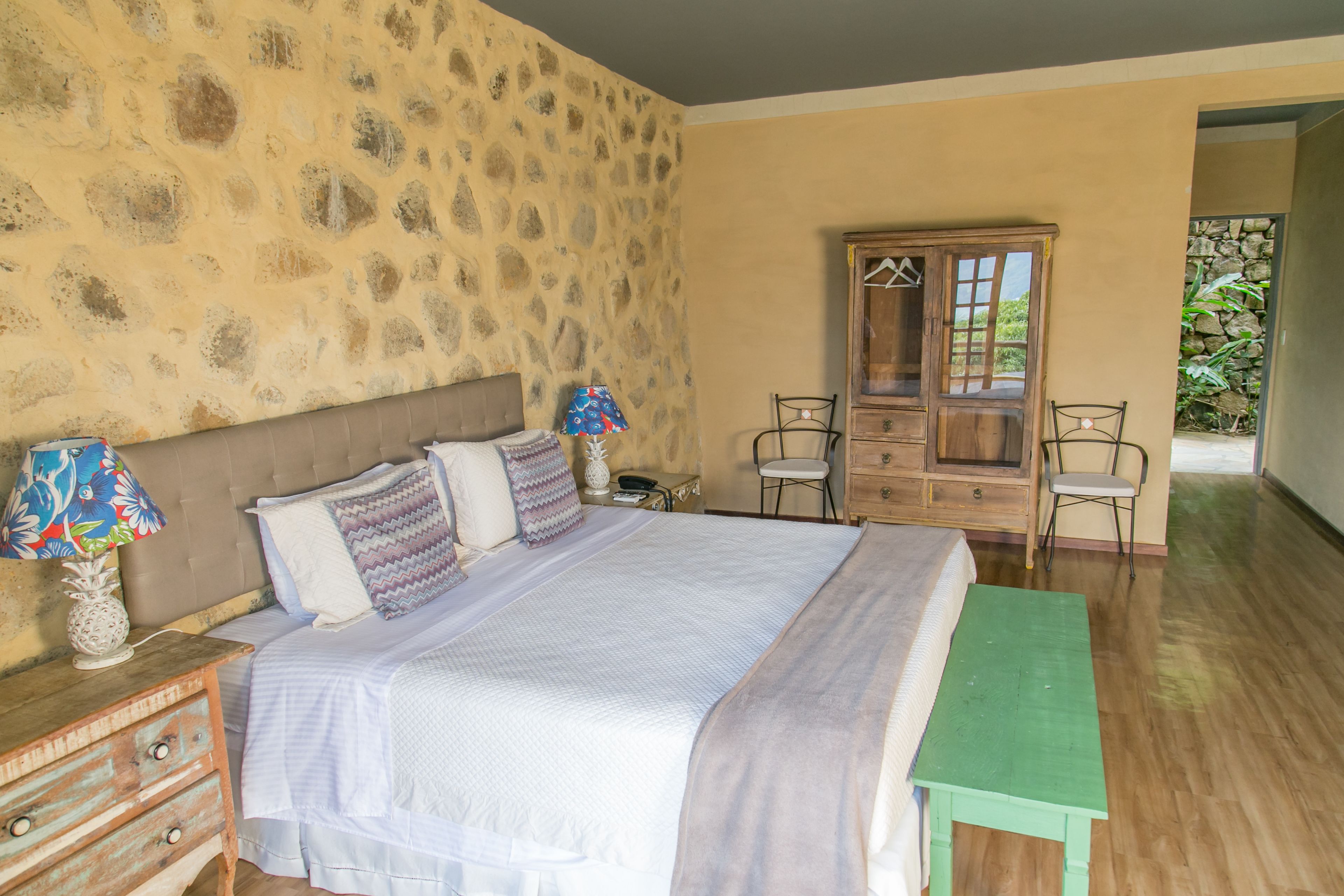 Ein Schlafzimmer mit einem großen Bett, einem hölzernen Schminktisch, einem Sessel und einer Bank.