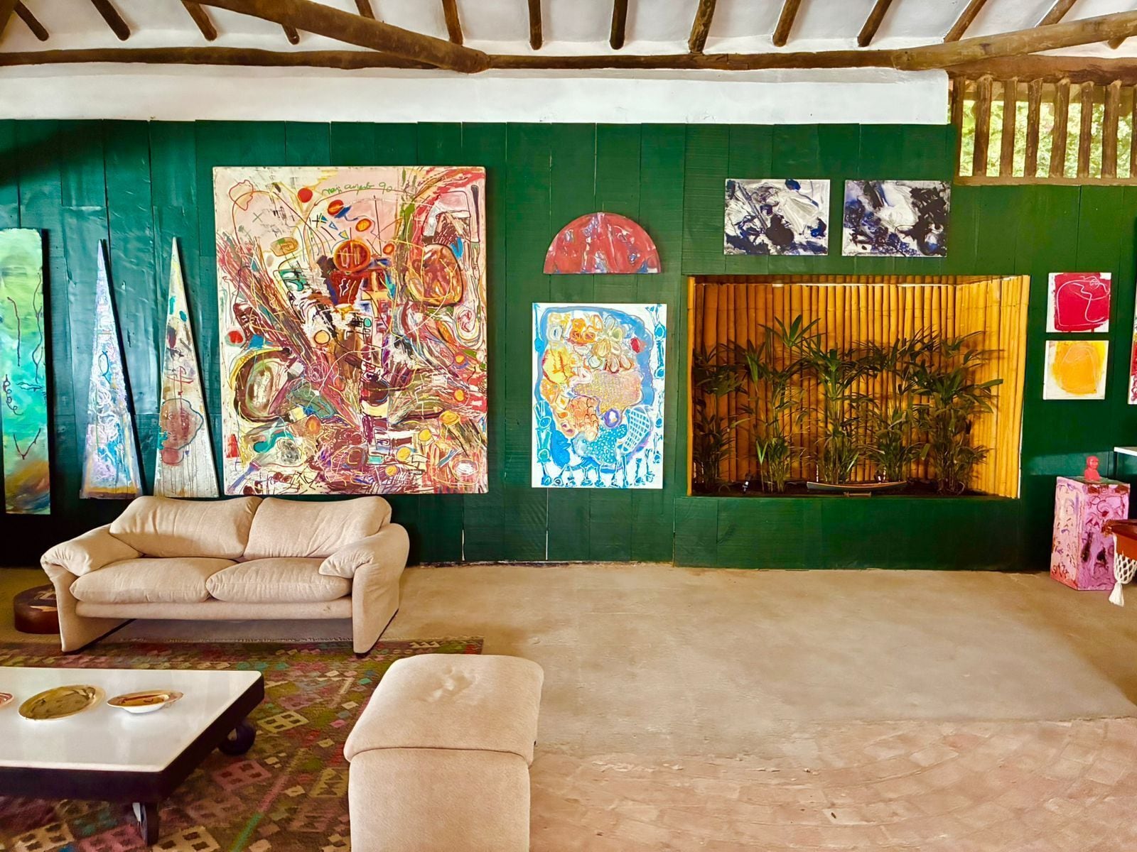 Une pièce avec un mur vert, un canapé blanc, un petit pouf et une table basse. On y trouve plusieurs tableaux et un paravent en bambou.