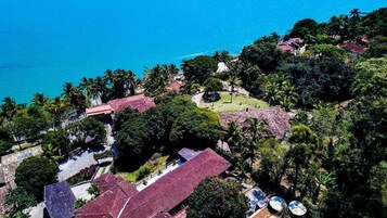 Vista aérea de una propiedad costera con varias construcciones, piscina y abundante vegetación.