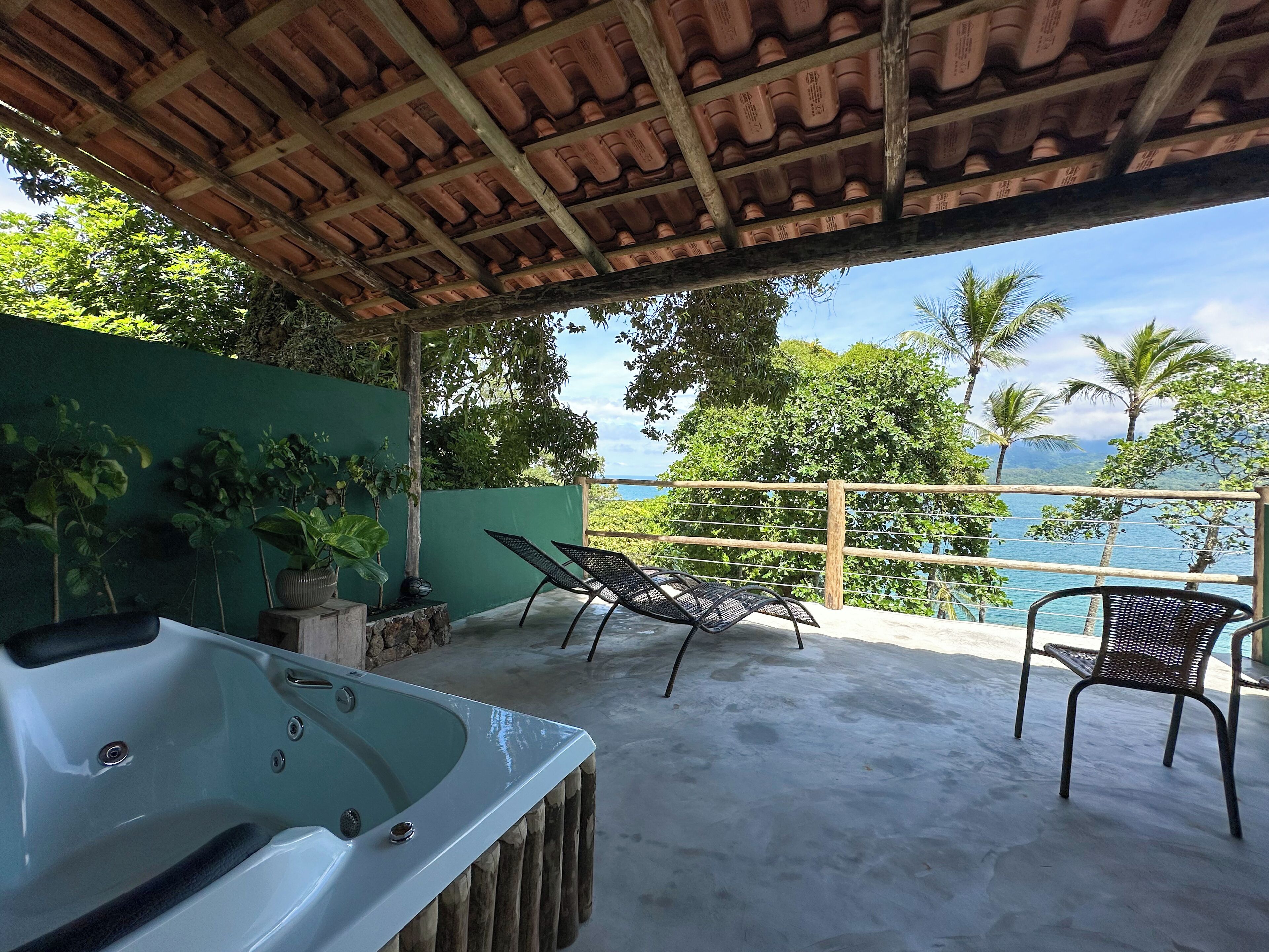 Un espacio al aire libre techado con un jacuzzi, sillones de descanso y vista al océano.