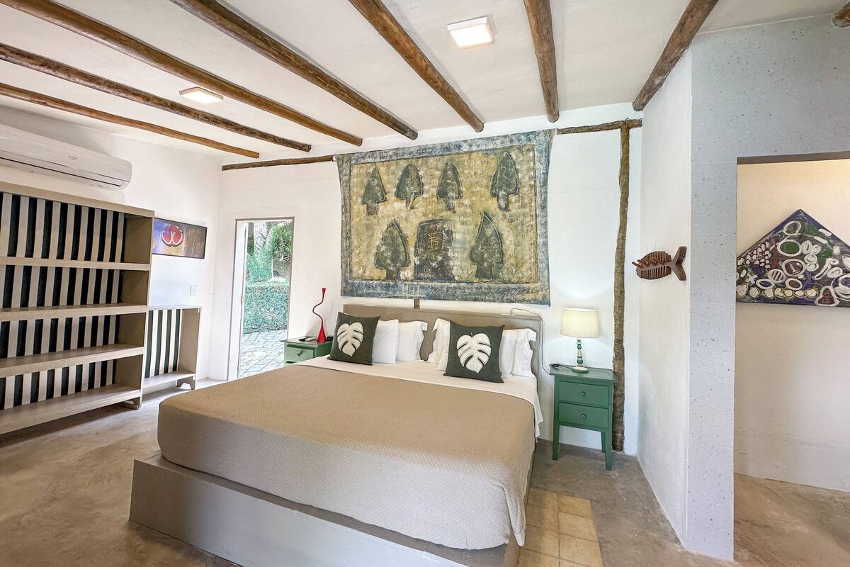 Een slaapkamer met een groot bed, een groen nachtkastje, een aan de muur hangend schilderij en een houten plank met gestreepte panelen.
