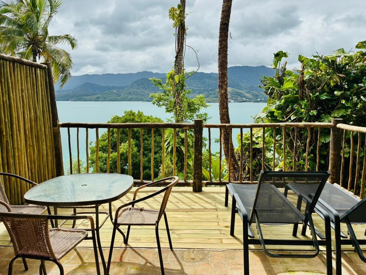 A deck with a table and chairs, overlooking a body of water and mountains.