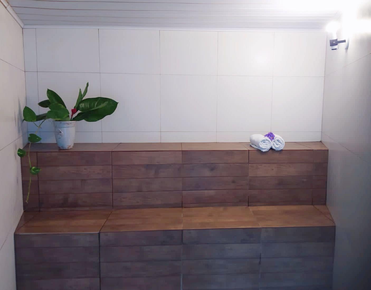 A bathroom with a wooden bench, a potted plant, and towels.