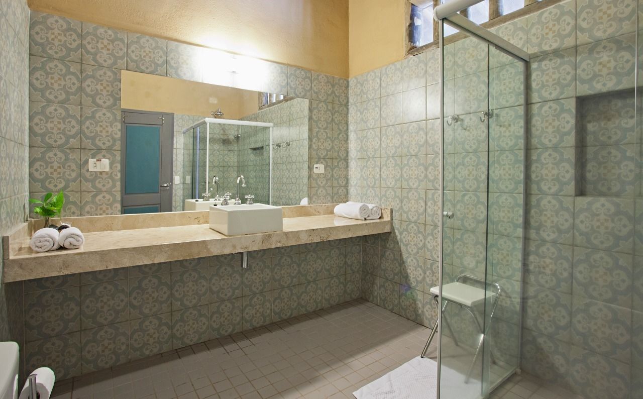 Un baño con baldosas estampadas, un espejo grande, un lavamanos y una cabina de ducha con mampara de vidrio.