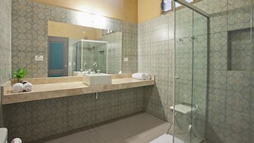 Un baño con baldosas estampadas, un espejo grande, un lavamanos y una cabina de ducha con mampara de vidrio.