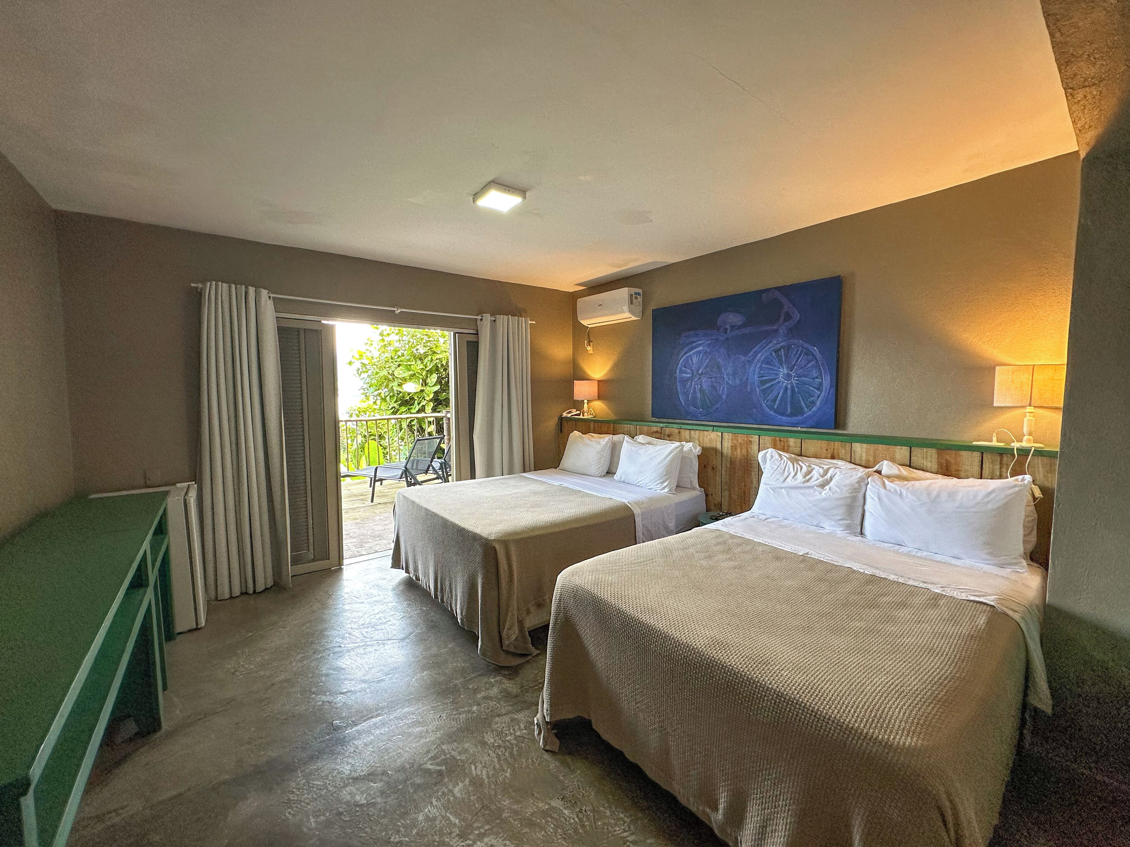 A hotel room with two beds, a balcony, a painting, and a green bench.